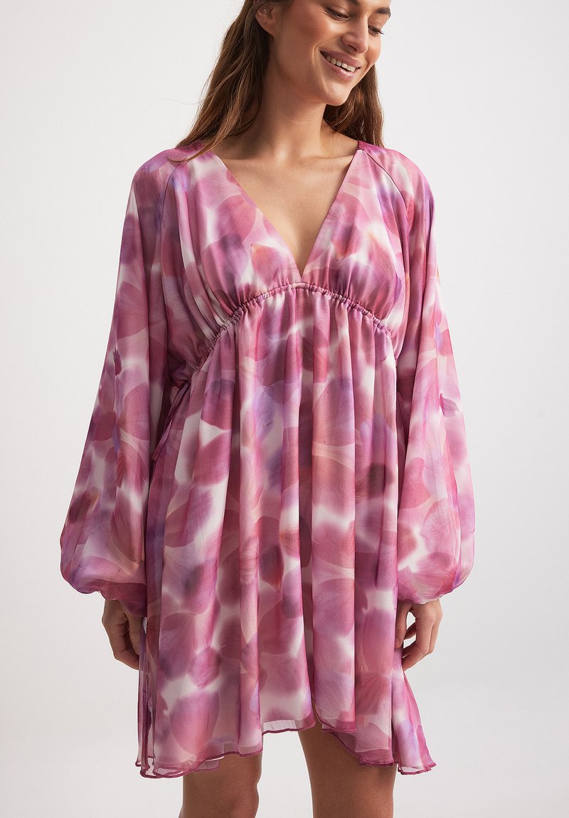 Abito fluido con scollo a V in un motivo floreale rosa e bianco, con maniche lunghe e morbide e una vita arricciata per un fit rilassato.