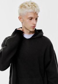 Felpa con cappuccio nera realizzata in tessuto morbido. Presenta una vestibilità ampia, spalle scese e polsini a costine. La felpa ha una tasca a marsupio.