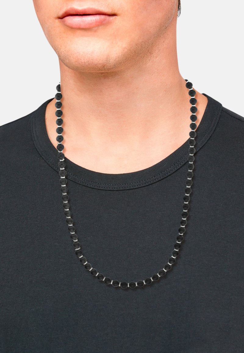 Collar de cuentas negras con cuentas redondas y hexagonales, exhibido en una persona que lleva una camisa negra. Textura suave, brillo sutil.