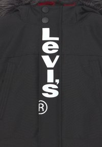 Svart vinterjacka med huva fodrad med syntetpäls, med en framträdande vit "Levi's"-logotyp framtill och dragkedjefickor.