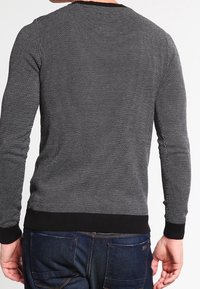 Pull à manches longues à motif noir et blanc avec un col rond et des poignets côtelés noirs, associé à un jean en denim bleu foncé.