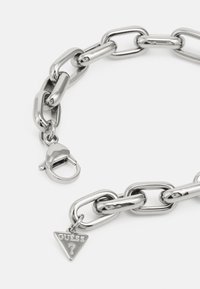 Metal chain necklace with large links, shiny silver finish. Features a lobster clasp and a triangular charm with the word "GUESS."