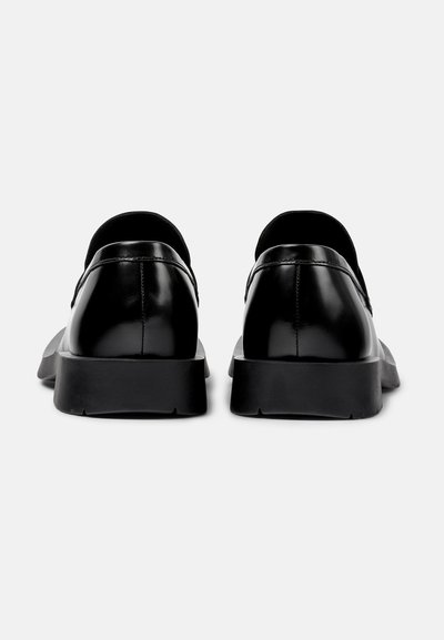 Chaussures en cuir noir avec une finition lisse, un dos arrondi, des semelles noires en caoutchouc basses et un design minimaliste. Pas de matériel ou d'accents visibles.