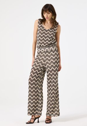 Ärmelloses Oberteil in Schwarz und Creme mit Zickzackmuster, kombiniert mit weiteren Hosen. Der Stoff scheint leicht und lässig mit einer glatten Textur zu sein.