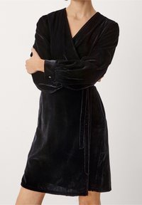 Svart sammet omslagsklänning med V-ringning, långa puffärmar och ett knytbälte. Mjuk textur, knälång, med en subtil lyster.