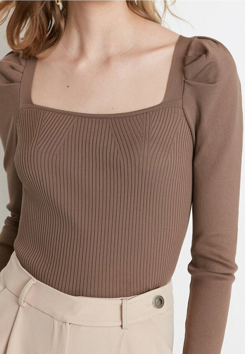 Braunes, geripptes Langarmoberteil mit quadratischem Ausschnitt und puffigen Schultern, getragen mit hochtaillierten beigen Hosen mit Knopfdetails.