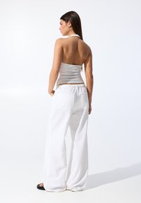 Pantaloni bianchi a gamba larga con vita elastica e tasche posteriori, abbinati a un top aderente in tessuto grigio chiaro con collo a halter. Texture liscia.