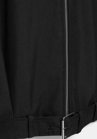 Krupan plan crnog dijela tkanine s okomitom srebrnom patentnim zatvaračem i podesivim remenom s metalnom kopčom na dnu.