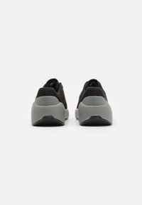 Scarpe sportive nere con suola grigia testurizzata, forma curva e collo imbottito. Presentano un design minimale e una linguetta posteriore.