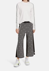 Hvid langærmet skjorte med grå mønstrede ærmer, kombineret med sorte og hvide mønstrede bukser med vide ben. Hvide sneakers med neonfarvede detaljer.