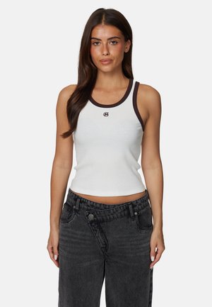 Biała prążkowana koszulka na ramiączkach z brązową kontrastową lamówką i logo na piersi, zestawiona z ciemnoszarymi, wysokim stanem jeansami.