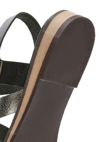 Sandal in pelle nera con accenti metallici, suola texturizzata e tacco in legno naturale. Dettaglio ravvicinato del motivo di grip della suola.