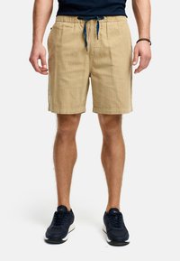 Beige bomuldsshorts med elastisk talje og sn�øre. Har sidelommer og en tekstureret overflade. Bæret med mørkeblå sneakers.