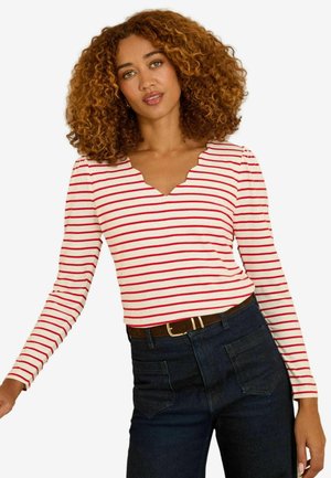 Red and white striped long-sleeve top with a scalloped neckline, paired with dark blue jeans and a brown belt. Features fitted design and smooth fabric.