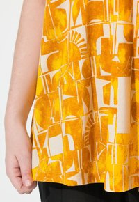 Tissu jaune à motifs avec des formes abstraites et un motif de soleil. Le matériau semble léger avec une texture lisse et une coupe décontractée.