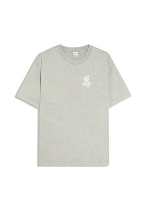 T-shirt gris clair à manches courtes avec un petit motif floral blanc et un texte en cursive sur le côté gauche de la poitrine.