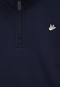 Tamsiai mėlyna džemperis su pusiau užtrauktuku ant kaklo. Turi mažą baltą siuvinėtą paukščio logotipą kairėje pusėje ir minkštą audinio tekstūrą.