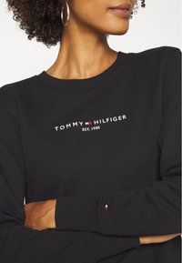 Felpa nera con logo ricamato "TOMMY HILFIGER EST. 1985". Polsini a costine con piccolo accento a bandiera. Tessuto morbido e strutturato.