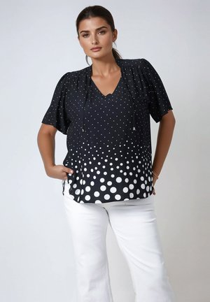 Blouse noire à manches courtes avec des pois blancs, dotée d'un col en V et d'un détail à cordon, motif dégradé se transformant en un uni au niveau de l'ourlet.