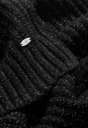 Fekete kötött anyag bordás textúrával, fehér fémes szálakkal, és egy apró ezüst fém címkével, amely jól láthatóan kiemelkedik.