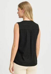 Čierny bezrukávový top s okrúhlym výstrihom, z mäkkého materiálu a so zvrásneným detailom na chrbte. Modelka má na sebe béžové nohavice.