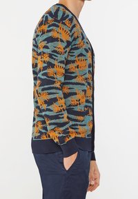 Stickad cardigan i marinblått med orange och teal lövmönster. Har V-hals, långa ärmar samt ribbade mudd och nederkant.