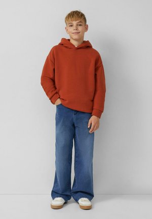 Orangener Kapuzenpulli mit Kängurutasche, kombiniert mit lockeren blauen Jeans und weißen Turnschuhen mit beiger Sohle. Einfaches, lässiges Outfit.