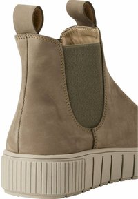 Bottines en suède beige avec une semelle nervurée, un panneau latéral élastique vert et des languettes de tirage au niveau du col. Texture lisse et design minimaliste.