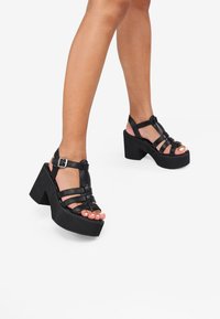 Sandalias de plataforma negras con suelas gruesas, diseño de tiras y cierre de hebilla. Textura de cuero suave con punta abierta.