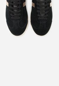 Sneakers in suede nero con lacci neri, caratterizzati da una striscia beige lungo il lato. Punta arrotondata e suola in gomma chiara.