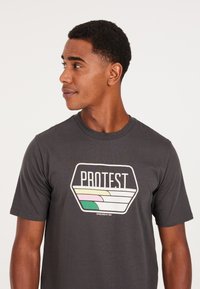 Grå bomulds t-shirt med en iøjnefaldende, multifarvet "PROTEST" grafik. Korte ærmer og en klassisk rund halsudskæring med blød tekstur.