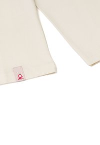 Krémový top s krátkým rukávem a ribbovanou strukturou, s malou růžovou značkovou nálepkou na lemu. Vhodný pro každodenní nošení díky svému volnému stylu.