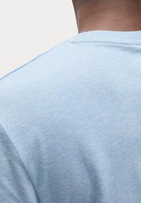 Camiseta de color azul claro de manga corta, hecha de una tela suave. Presenta un cuello redondo con una textura lisa y un sutil patrón jaspeado en el material.