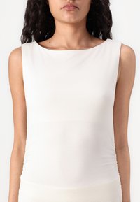 Κρεμ φανελάκι χωρίς μανίκια με μαλακό και ελαστικό ύφασμα. Στρογγυλή λαιμόκοψη και φρουτοί λεπτομέρειες στα πλάγια.