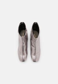 Botines metálicos plateados con punta afilada, cremallera lateral y acabado suave. Presentan un tacón bajo y líneas limpias y elegantes.