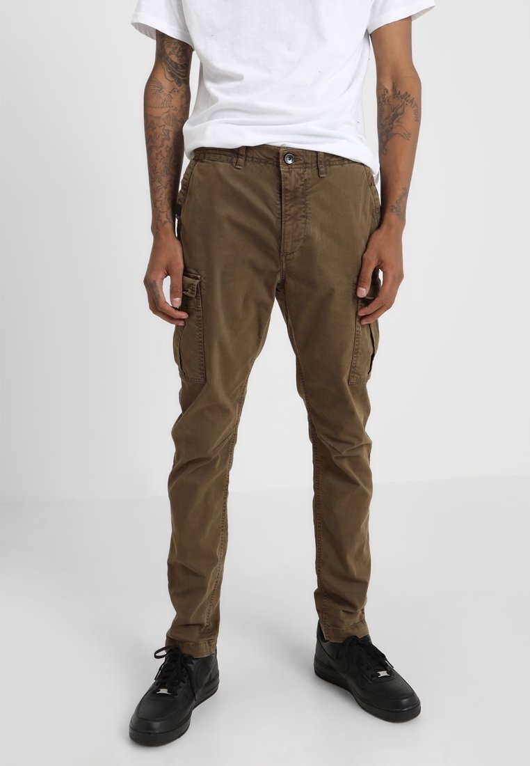 Pantalon cargo marron en coton, doté de poches latérales et d'une coupe slim. Porté avec un t-shirt blanc et des baskets noires.