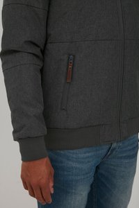 Gray zip-up jacket with textured fabric, ribbed cuffs and hem, features a side zip pocket with contrasting brown hardware.
