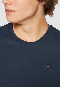Navy blue cotton T-shirt with a round neckline and short sleeves, featuring a small embroidered logo in red, white, and blue on the chest.