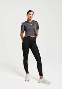 Grijze cropped t-shirt met "Redmax" logo, gecombineerd met hoge zwarte leggings. Outfit compleet met witte sneakers. Eenvoudig ontwerp.