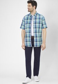 Kortblauwe en groene geruite overhemd met korte mouwen, gecombineerd met donkerblauwe jeans en witte sneakers. Beschikt over knopen en een casual pasvorm.