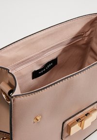 Krémová kabelka s hladkým povrchem, obsahující zipovou kapsu, zlatý kovový uzávěr a štítek "NEW LOOK" uvnitř.