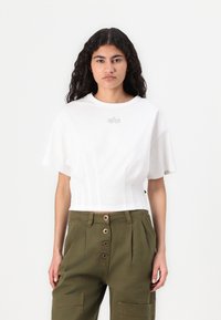 Valkoinen lyhythihainen crop-top, jossa on hillitty kohokuviointi rinnassa. Yhdistetty oliivinvihreisiin korkeavyötäröisiin housuihin.