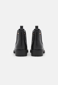 Černé kotníkové boty s texturovaným svrškem z imitace kůže, černými elastickými bočními panely a plochou gumovou podrážkou. Mají poutka na zadní straně a dekorativní nýty.