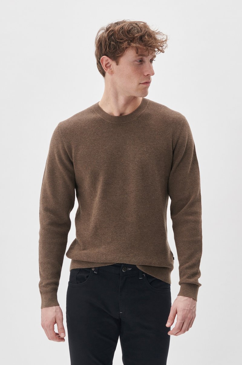 Brauner gestrickter Pullover mit Rundhalsausschnitt und langen Ärmeln, kombiniert mit schwarzen Hosen. Weiche Textur und gerippte Bündchen.