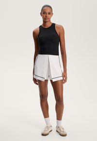 Fekete bordázott ujjatlan felső kerek nyakkivágással, fehér, fekete díszítésű és redőzött részletekkel ellátott sorttal párosítva. Sportcipők és fehér zoknik teszik teljessé a megjelenést.