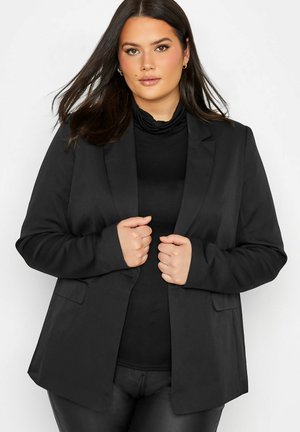 Sort blazer med en skræddertilpasset pasform, normale lapels og to forlommer, båret over en sort turtle neck. Glat stof med en mat finish.