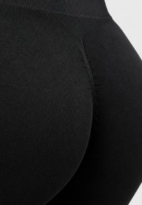 Gros plan sur un legging noir sans couture avec un détail de couture incurvée et un tissu texturé au niveau des hanches.