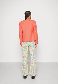 Veste corail à épaules structurées, associée à un pantalon évasé multicolore orné d'un motif tourbillonnant, portée avec des chaussures à plateforme.