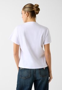 Wit T-shirt met korte mouwen van zacht katoen; losse pasvorm met een ronde hals, voorzien van een eenvoudig ontwerp en een gladde textuur.