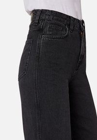 Černé džínové kalhoty s vysokým pasem a přiléhavým střihem, které mají klasický pětikapsový design a jemné detaily prošití.